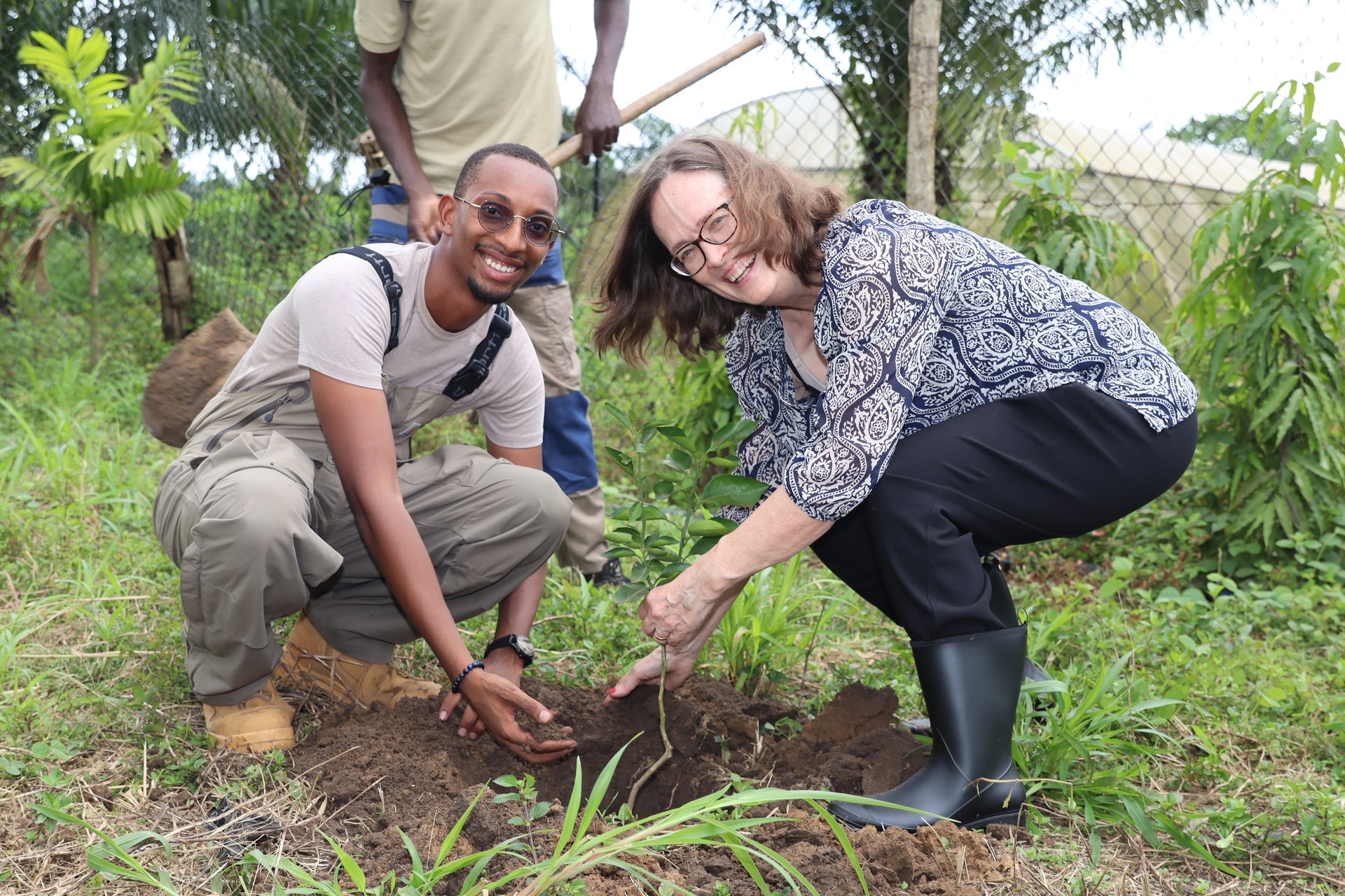 Two participants collaborate while planting a tree during an environmental activity.