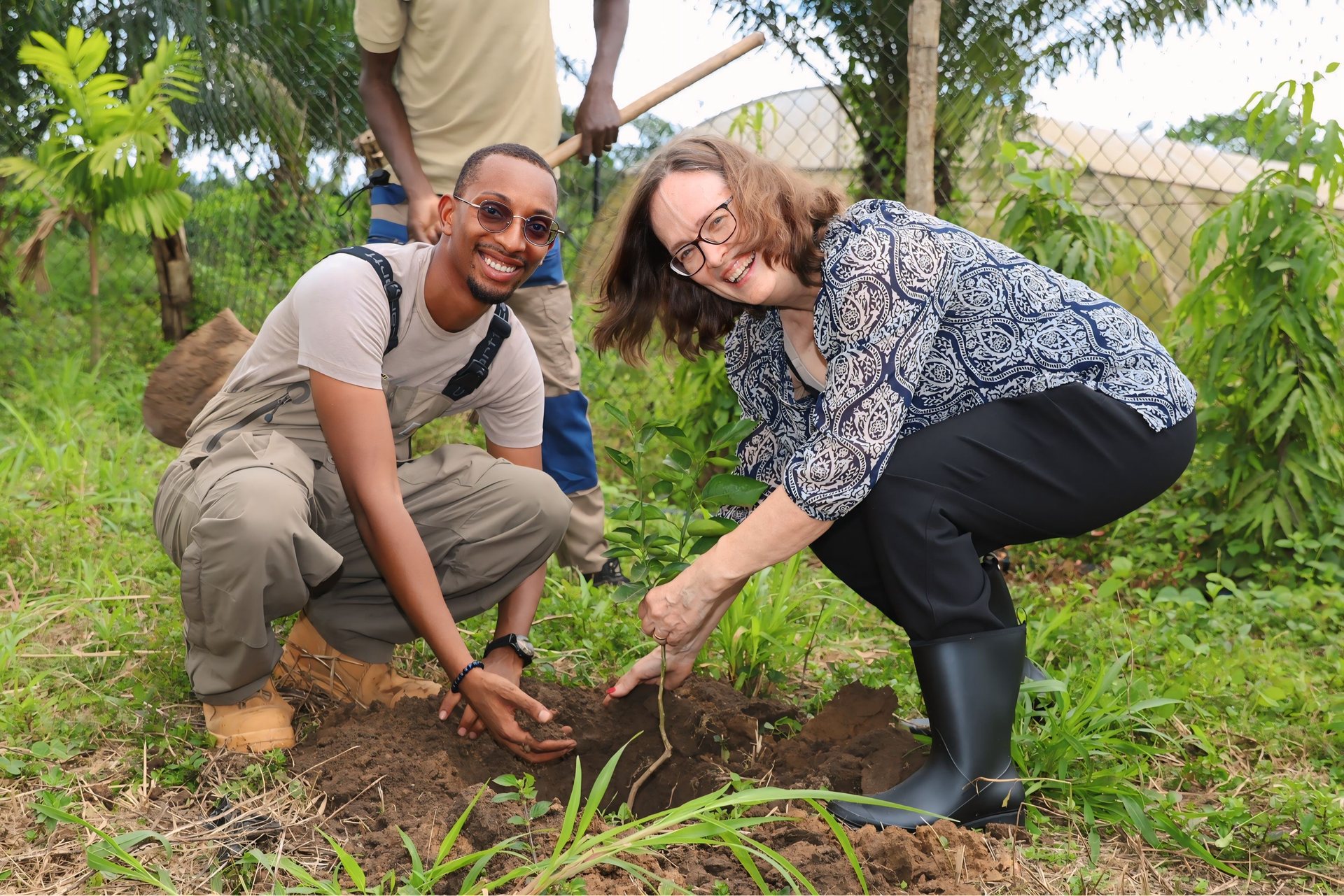 Two participants plant a young tree during an outdoor environmental activity.